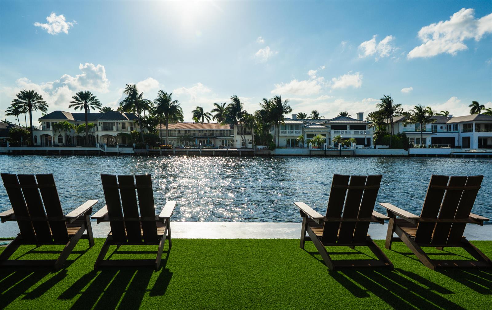Four wooden chairs sit on a green lawn overlooking a canal lined with waterfront homes — 1075 Spanish River Road, Boca Raton FL 33432, BOCA RATON, FL