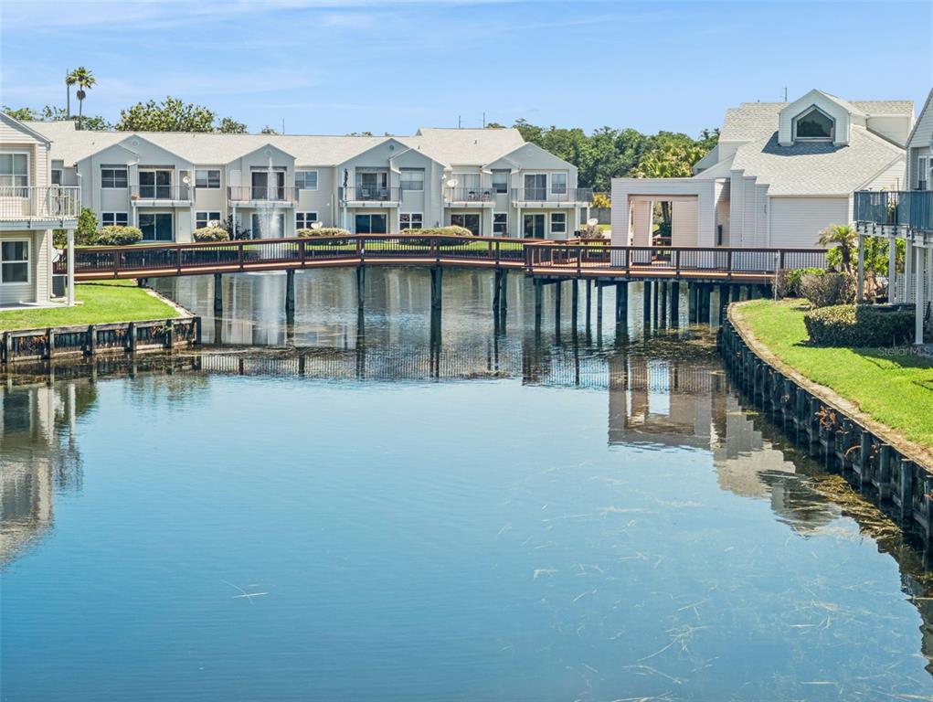 A wooden footbridge spans a pond in front of multi-story apartment buildings — 2564 WOODGATE BOULEVARD UNIT 204, ORLANDO, FL