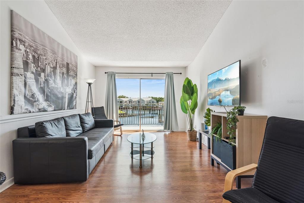 A living room features a black sofa, glass coffee table, and sliding doors overlooking water — 2564 WOODGATE BOULEVARD UNIT 204, ORLANDO, FL