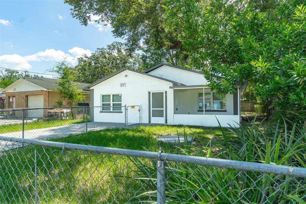 A white single-story house with a screened-in porch stands behind a chain-link fence — 8115 N SEMMES STREET, TAMPA, FL