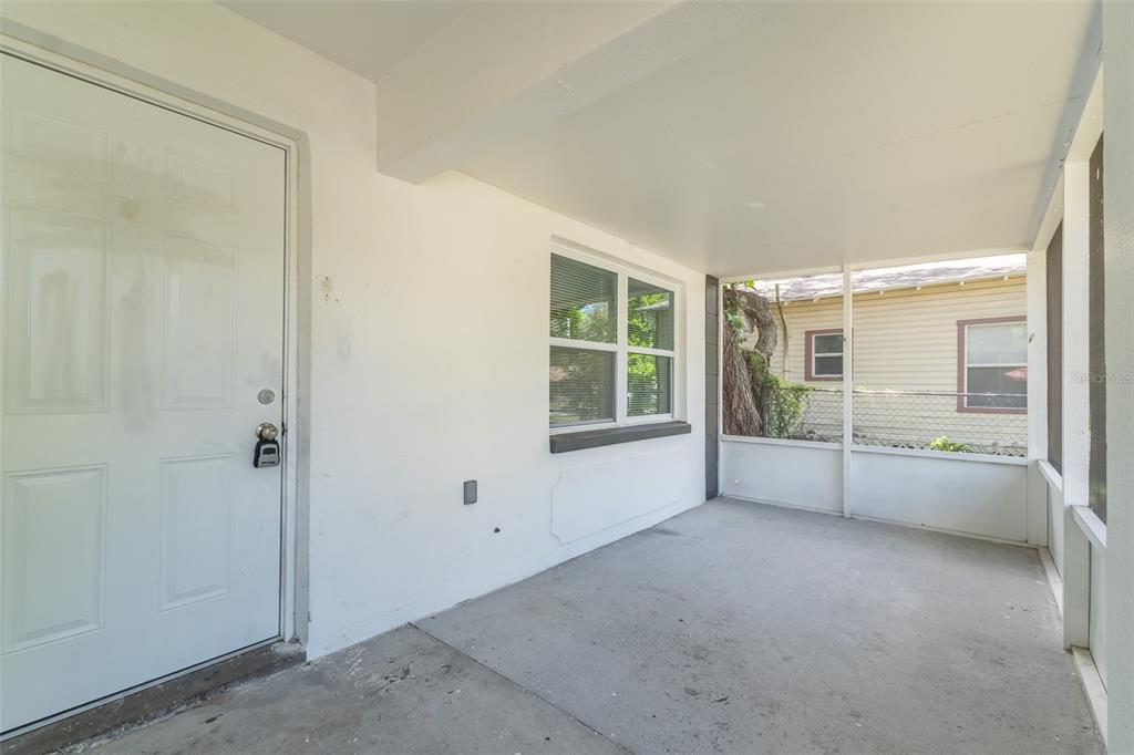 A covered, screened-in porch features a white door, a window, and a concrete floor — 8115 N SEMMES STREET, TAMPA, FL
