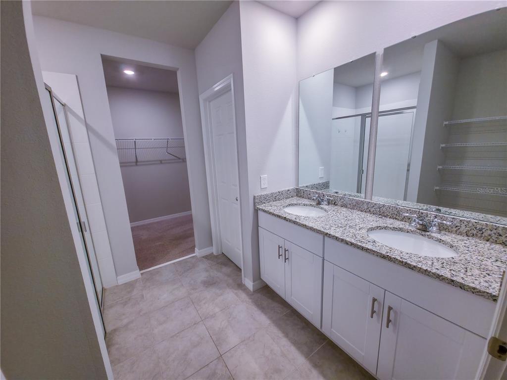 A bathroom features a double vanity with granite countertops, white cabinets, and a walk-in closet — 3301 WEITZEL DRIVE, HAINES CITY, FL