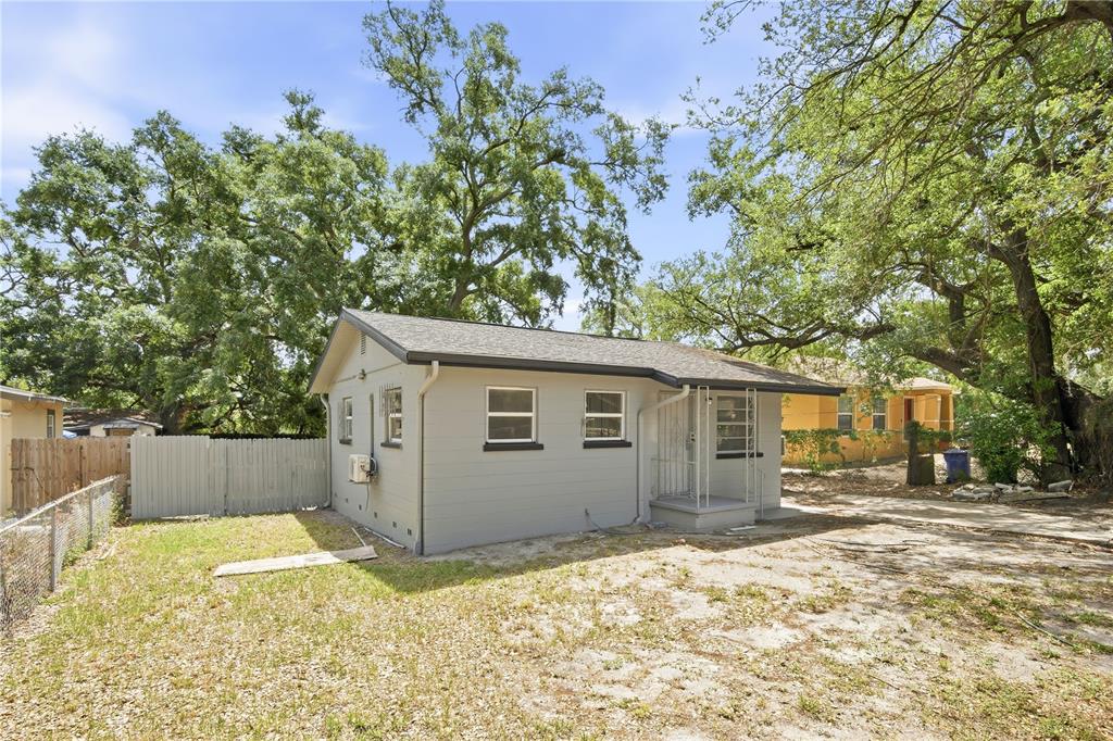 A gray, single-story house with a shingled roof sits on a sandy lot with trees — 6209 N 43RD STREET, TAMPA, FL