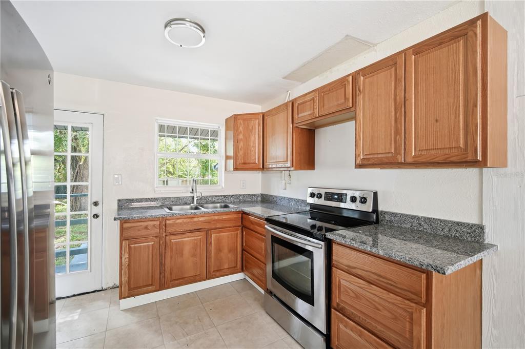 A kitchen features wood cabinets, granite countertops, stainless steel appliances, and a glass-paneled exterior door — 6209 N 43RD STREET, TAMPA, FL