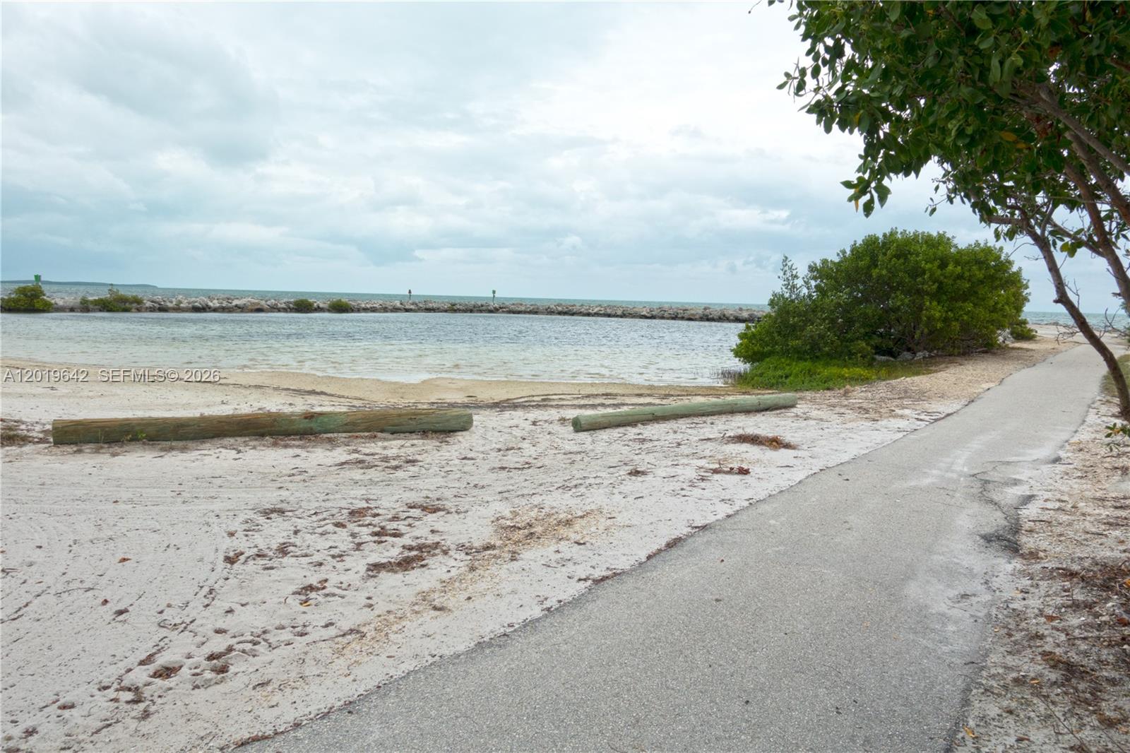 A paved path runs alongside a sandy beach area with wooden logs and a rock jetty — 8 Ocean View Blvd, Key Largo FL 33037, KEY LARGO, FL