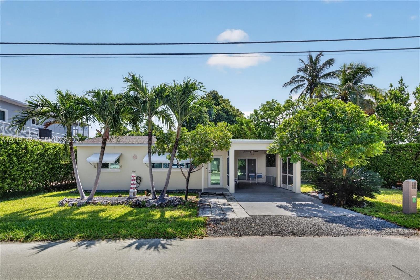 A single-story house with a carport, palm trees, and a lawn under a blue sky — 8 Ocean View Blvd, Key Largo FL 33037, KEY LARGO, FL