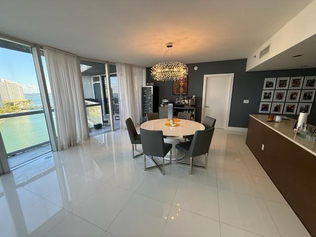 A dining area features a round table, modern chairs, a chandelier, and floor-to-ceiling windows — 465 Brickell Avenue # 1201, Miami FL 33131, MIAMI, FL