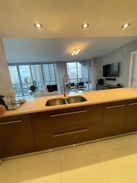 A kitchen island with a double sink overlooks a living area with floor-to-ceiling windows — 465 Brickell Avenue # 1201, Miami FL 33131, MIAMI, FL