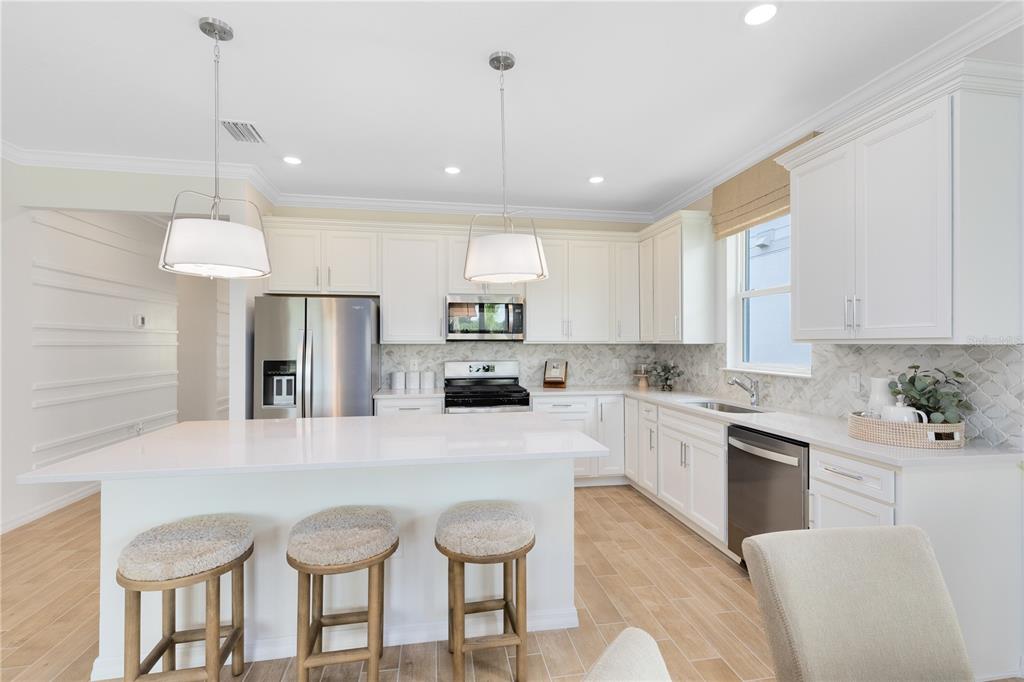 A bright kitchen features white cabinetry, a large island with three stools, and stainless appliances — 4980 GOOD DAY LANE, WEST MELBOURNE, FL