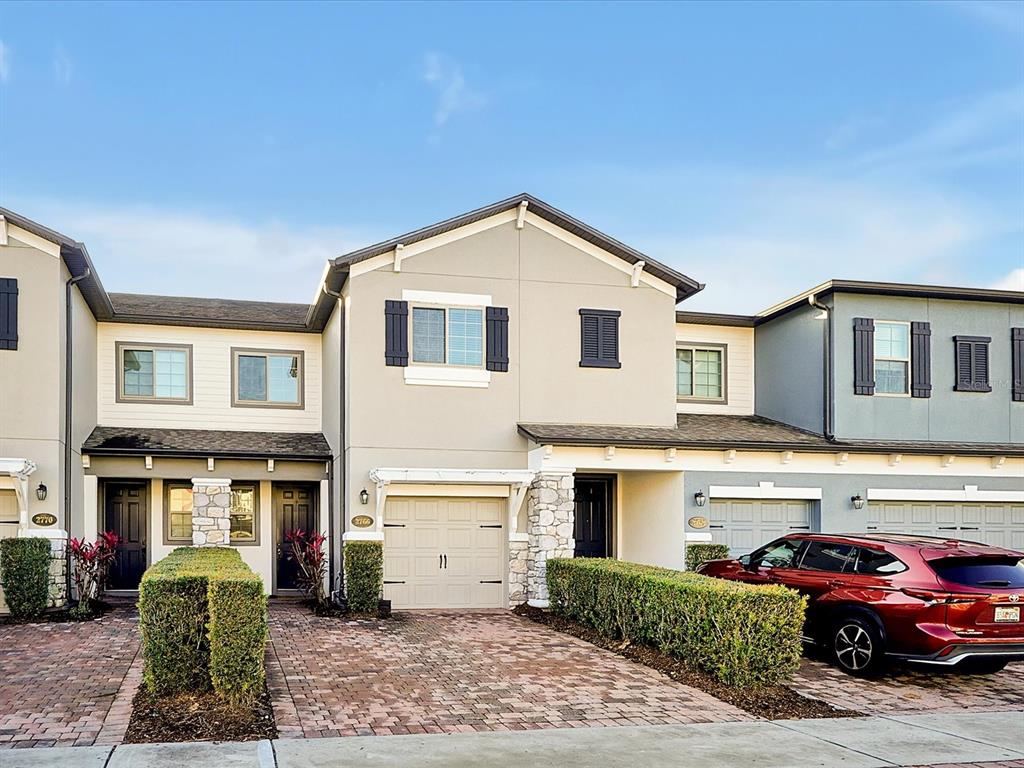 A row of three-story townhouses with beige and gray facades, brick driveways, and manicured hedges — 2766 WHITE ISLE LANE, ORLANDO, FL