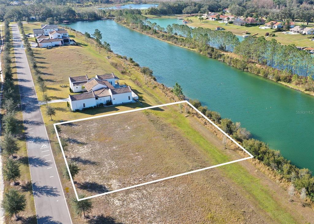 An aerial view shows a vacant rectangular lot bordering a canal next to a house — 13085 SWINNEY LANE, CLERMONT, FL