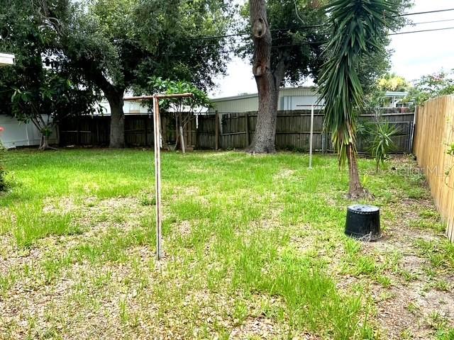 A grassy backyard features a clothesline, mature trees, and a wooden fence — 10964 84TH AVENUE, SEMINOLE, FL