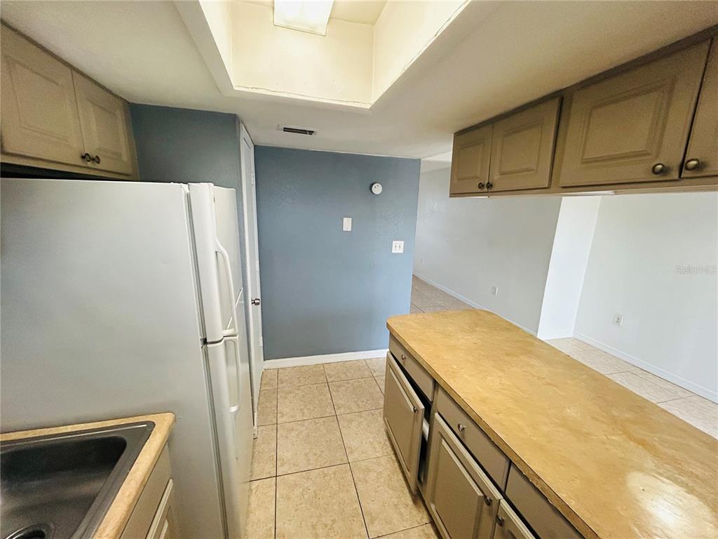 A kitchen features light-colored cabinets, a white refrigerator, a tiled floor, and a breakfast bar — 2775 L B MCLEOD ROAD UNIT B, ORLANDO, FL