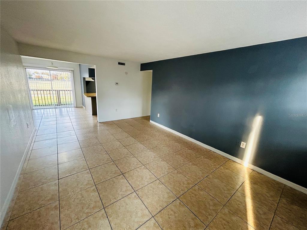 An empty living room features tan tile flooring, a dark blue accent wall, and sliding doors — 2775 L B MCLEOD ROAD UNIT B, ORLANDO, FL
