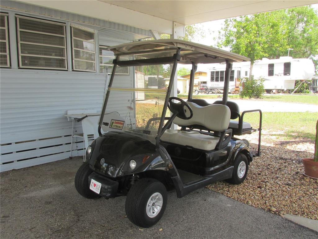A black golf cart is parked under a carport next to a mobile home — 7 BLUE QUILL CIRCLE, LAKE WALES, FL