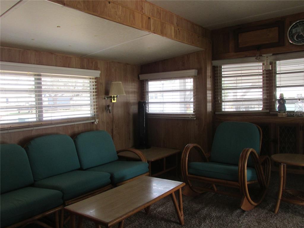 A living room features wood-paneled walls, teal cushioned furniture, and several windows with blinds — 7 BLUE QUILL CIRCLE, LAKE WALES, FL