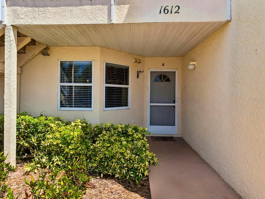 The exterior of a ground-floor apartment unit features a screen door and a small walkway — 1612 FAIRWAY TRACE UNIT A, PALMETTO, FL