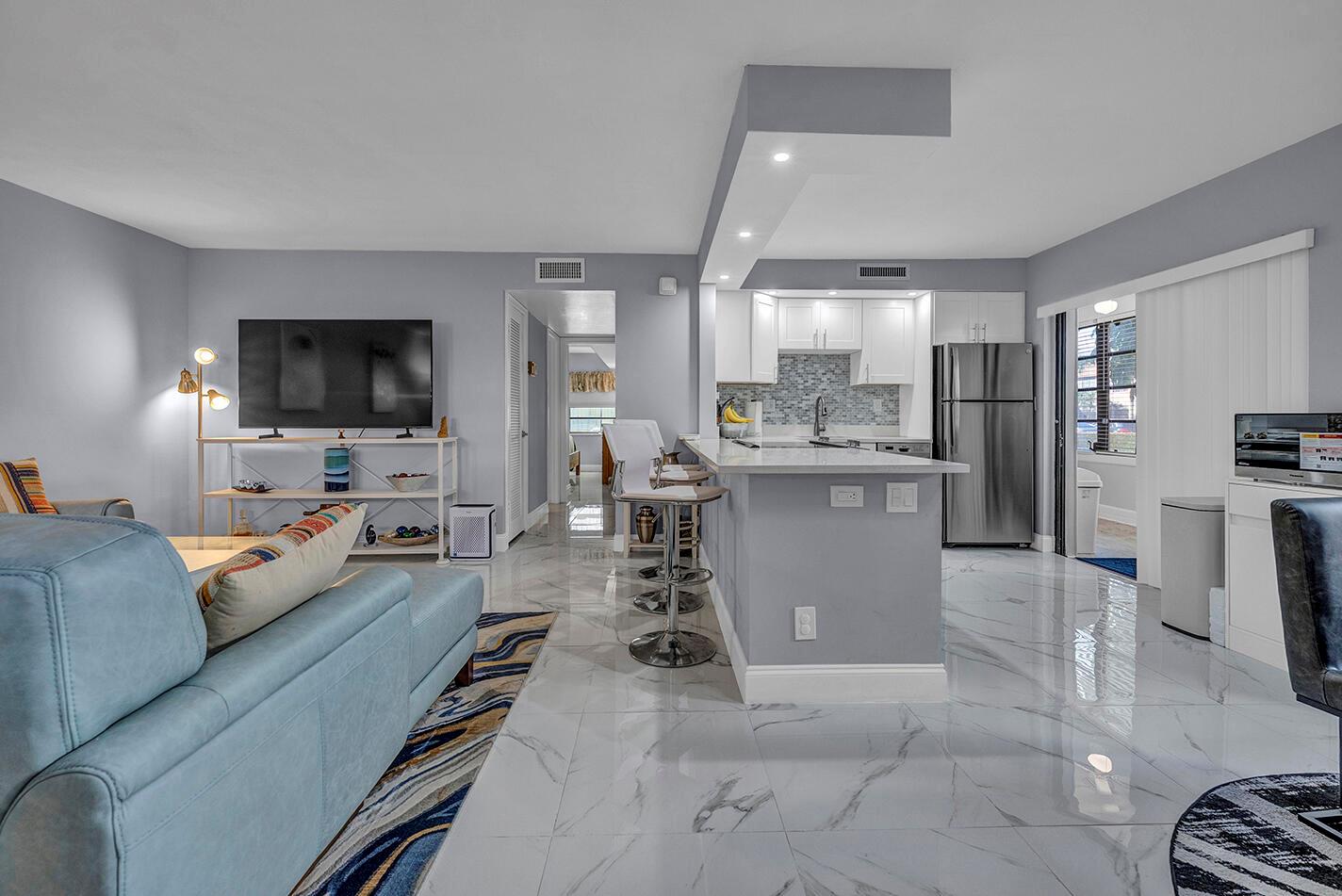 An open-concept living room and kitchen featuring light gray walls, white cabinets, and marble-look flooring — 162 Capri D, Delray Beach FL 33484, DELRAY BEACH, FL