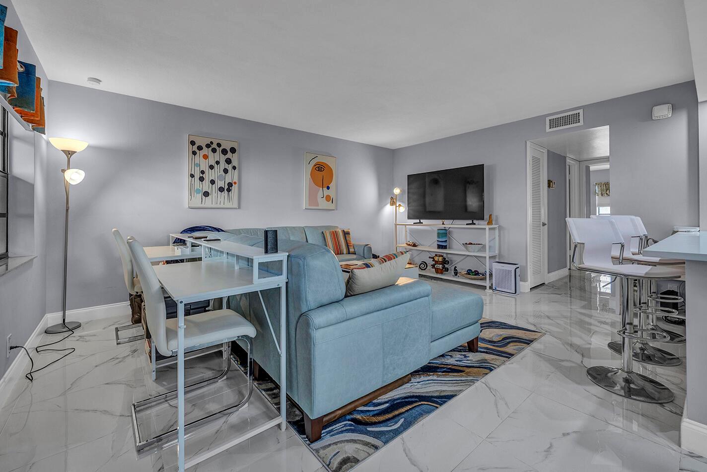 A living room features a blue sectional sofa, a white desk, and white marble flooring — 162 Capri D, Delray Beach FL 33484, DELRAY BEACH, FL