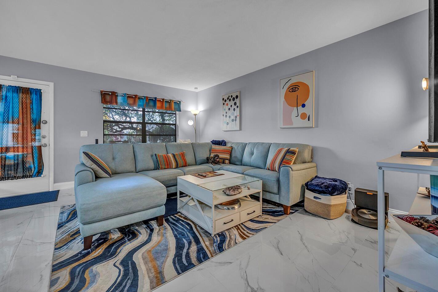 A living room features a light blue sectional sofa, a glass-topped coffee table, and patterned rug — 162 Capri D, Delray Beach FL 33484, DELRAY BEACH, FL