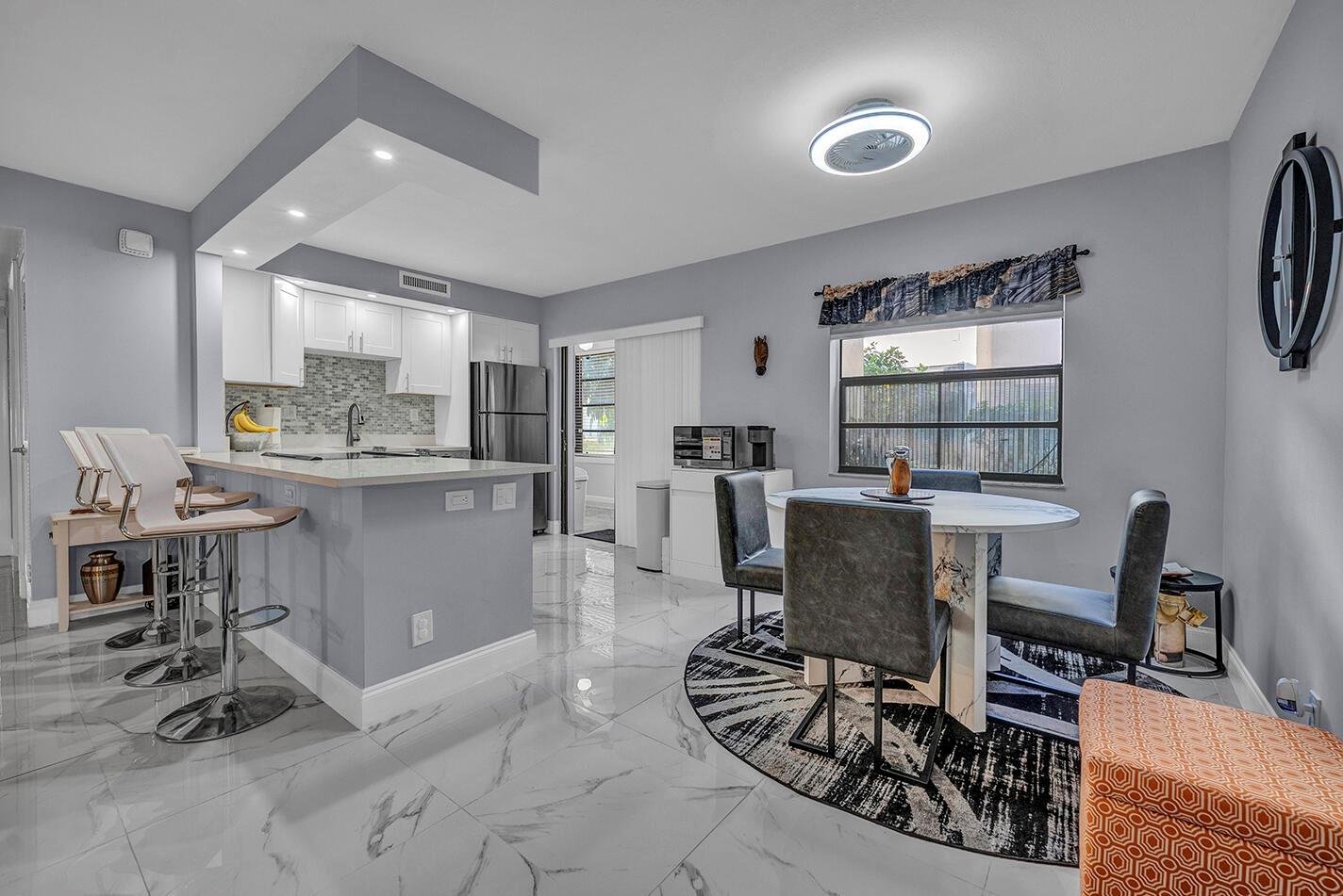 A modern kitchen and dining area with white cabinets, marble-look tile floors, and gray walls — 162 Capri D, Delray Beach FL 33484, DELRAY BEACH, FL