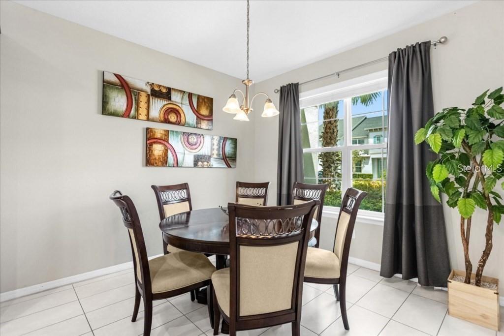 A dining room features a round wooden table, four chairs, abstract wall art, and curtains — 1540 CAREY PALM CIRCLE, KISSIMMEE, FL