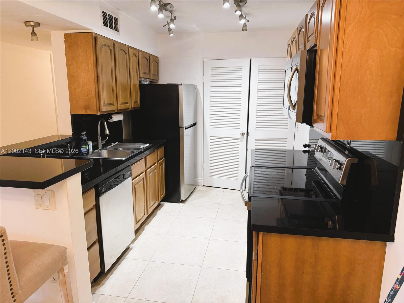 A kitchen features wood cabinets, black countertops, stainless steel appliances, and light-colored tile flooring — 7483 SW 82nd St # A102, Miami FL 33143, MIAMI, FL