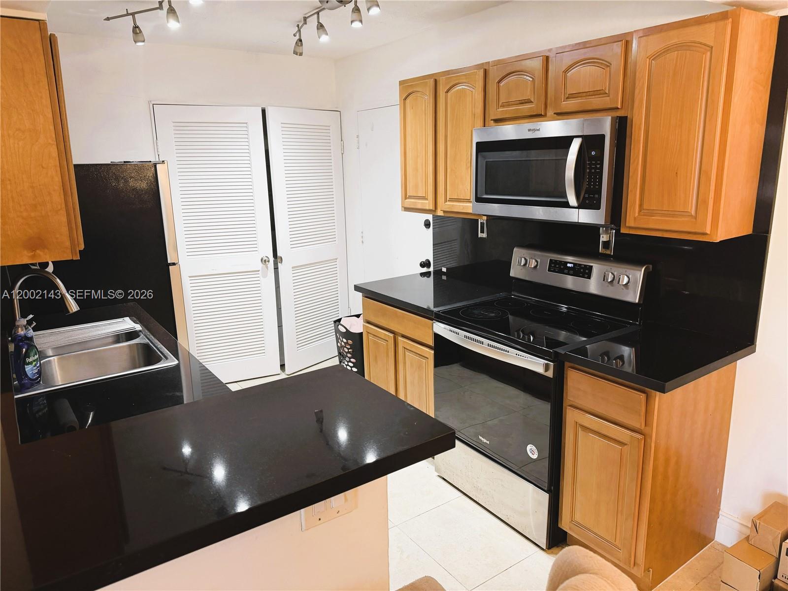 A kitchen features wood cabinets, black countertops, stainless steel appliances, and white louvered doors — 7483 SW 82nd St # A102, Miami FL 33143, MIAMI, FL