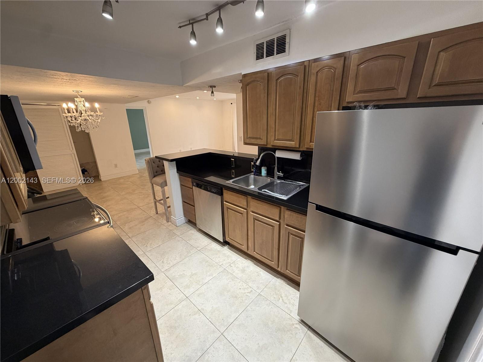 A kitchen features wood cabinets, black countertops, stainless steel appliances, and light-colored tile flooring — 7483 SW 82nd St # A102, Miami FL 33143, MIAMI, FL