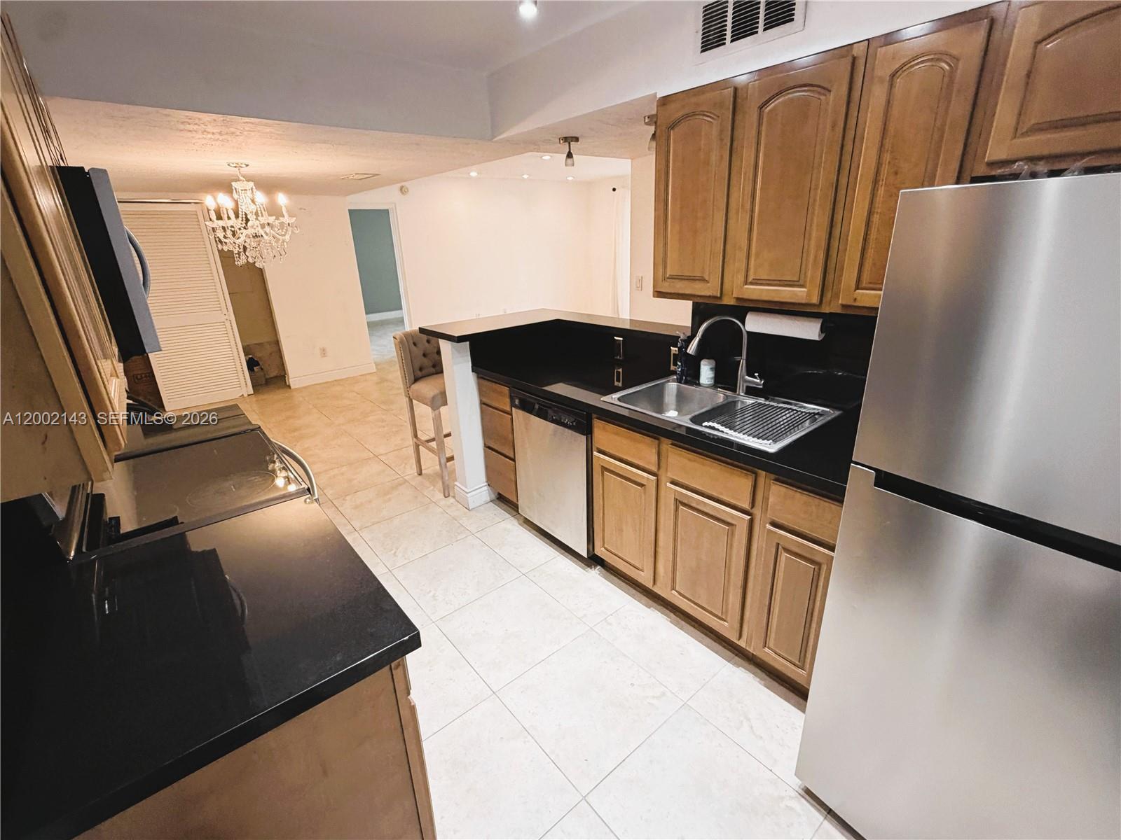 A kitchen features wood cabinets, black countertops, stainless steel appliances, and tile flooring — 7483 SW 82nd St # A102, Miami FL 33143, MIAMI, FL