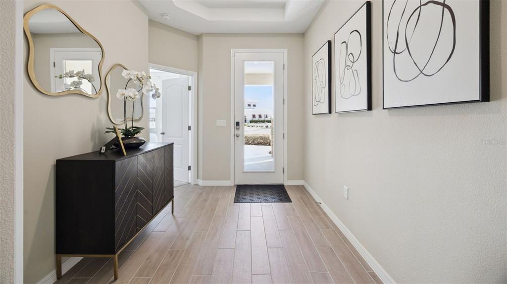 An entryway features light wood-look tile flooring, a dark console table, mirrors, and abstract wall art — 3050 KINGSMAN TRAIL, ORMOND BEACH, FL
