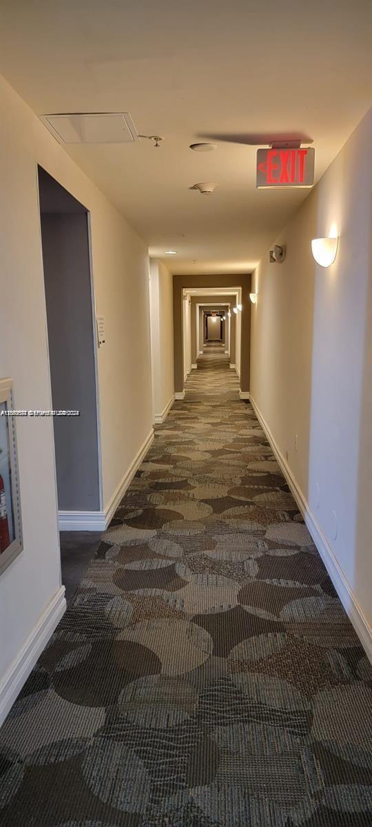 A long, narrow apartment hallway features patterned carpet, white walls, and recessed lighting — HOLLYWOOD, FL
