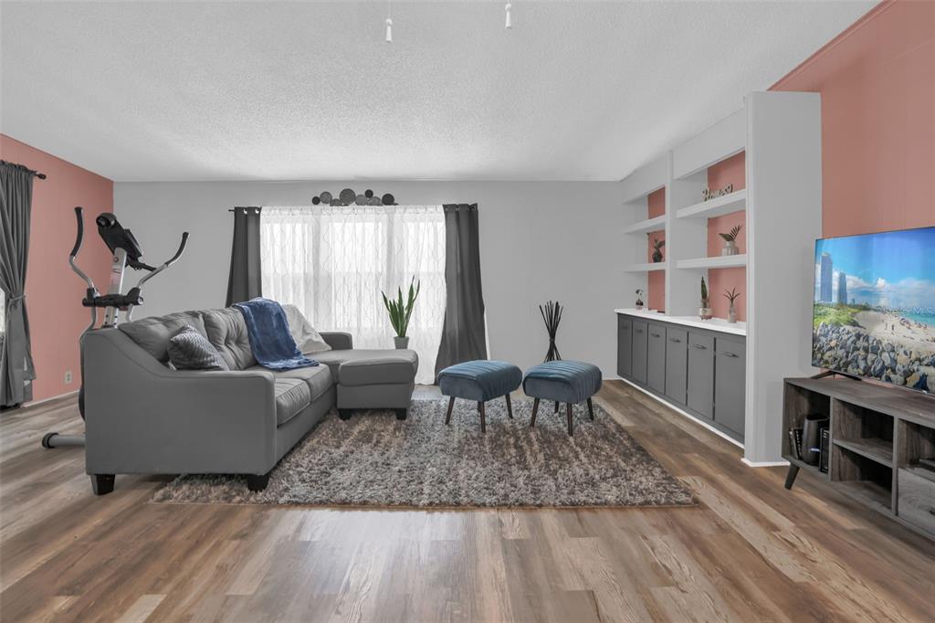 A living room features gray flooring, a sectional sofa, built-in shelving, and pink accent walls — 6666 BRIARHILL DRIVE NE, WINTER HAVEN, FL