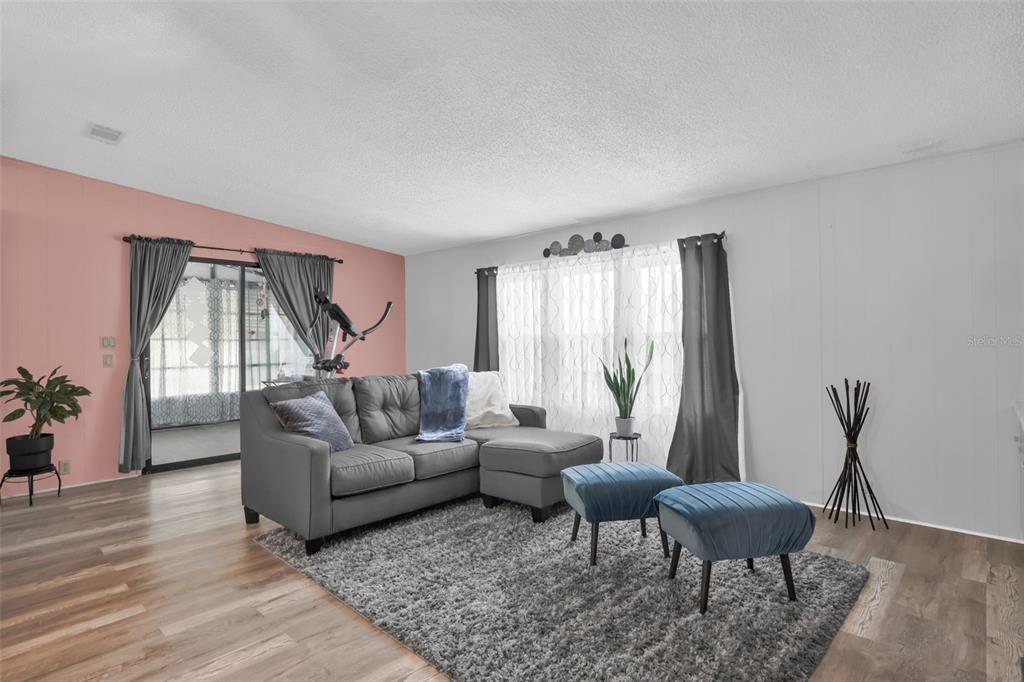 A living room features a gray sectional sofa, two blue ottomans, and a pink accent wall — 6666 BRIARHILL DRIVE NE, WINTER HAVEN, FL