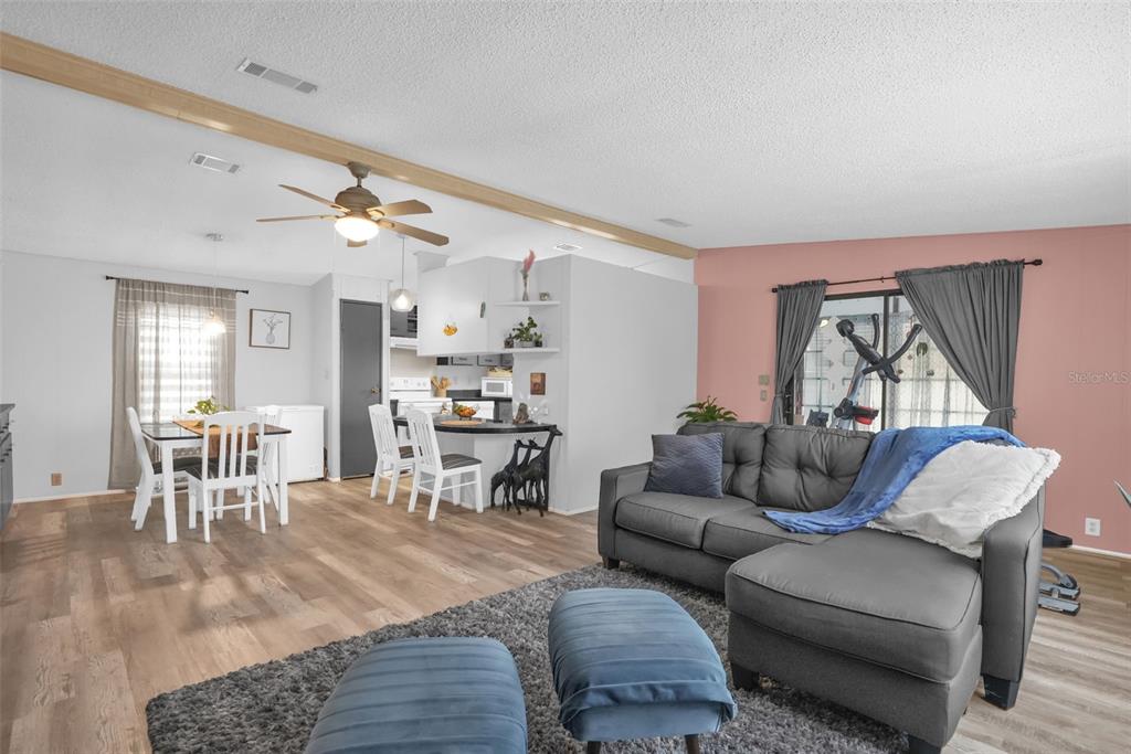 An open-concept living and dining area features wood-look flooring, a gray sectional, and kitchen access — 6666 BRIARHILL DRIVE NE, WINTER HAVEN, FL