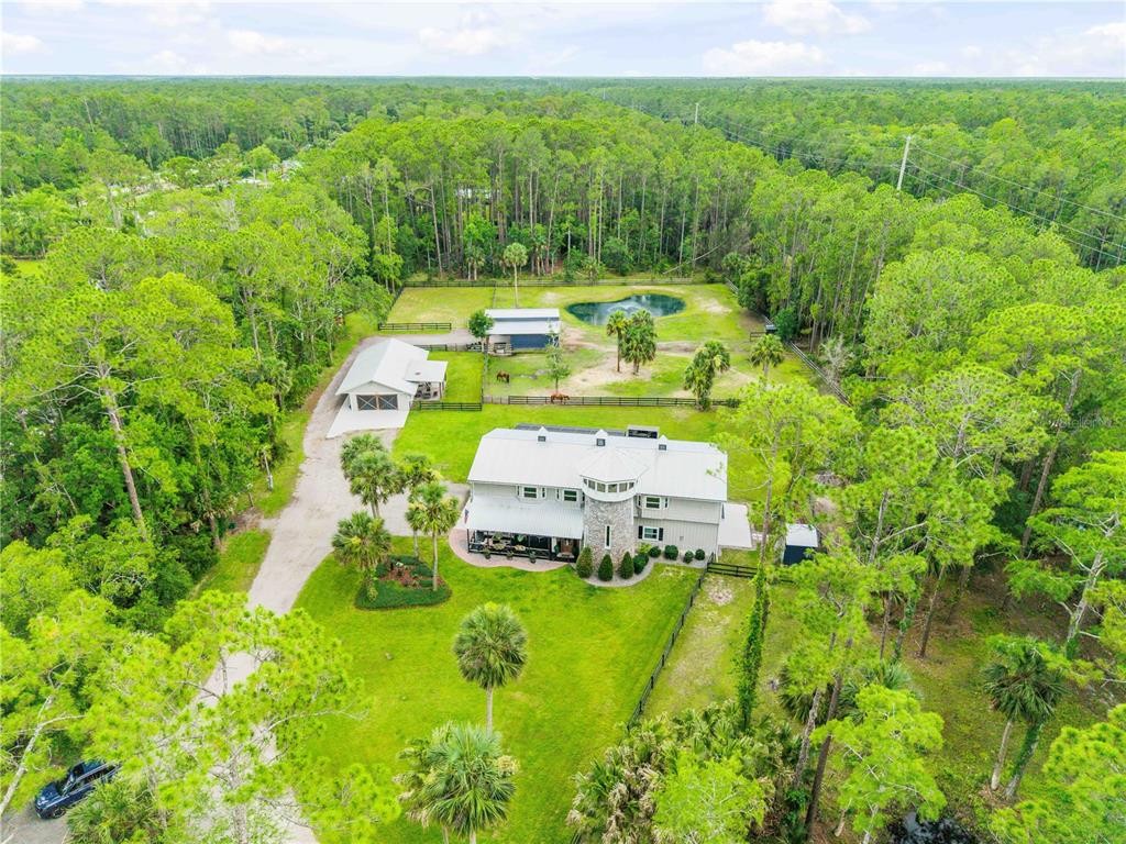 An aerial view shows a large house with a metal roof, outbuildings, and a pond — 2195 W POINSETTIA DRIVE, PORT ORANGE, FL