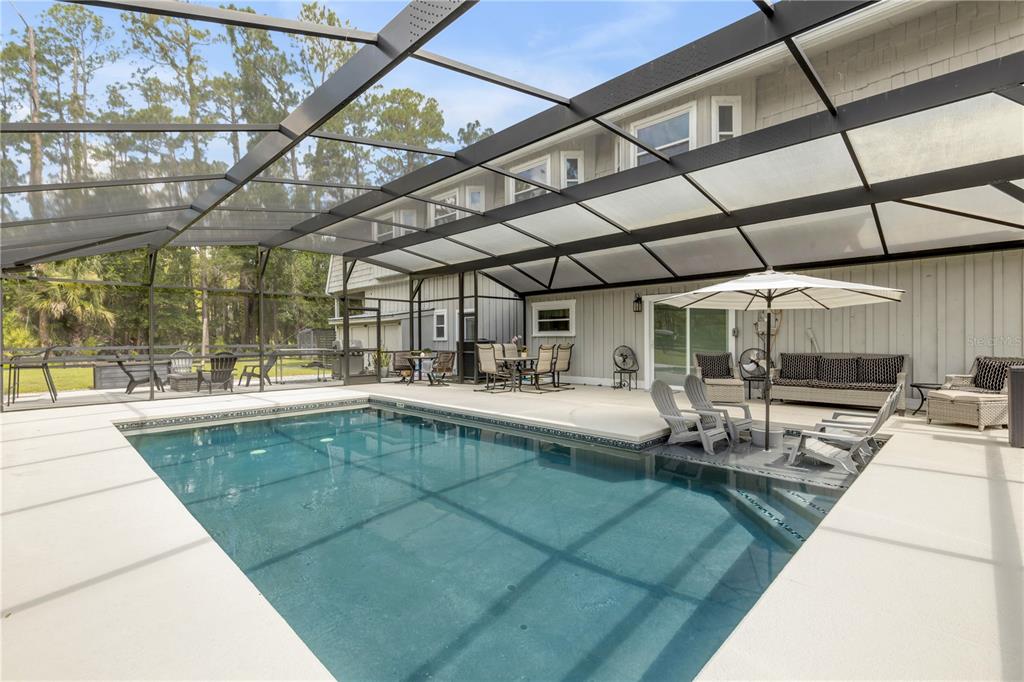A screened-in patio features a rectangular swimming pool, outdoor furniture, and a white umbrella — 2195 W POINSETTIA DRIVE, PORT ORANGE, FL