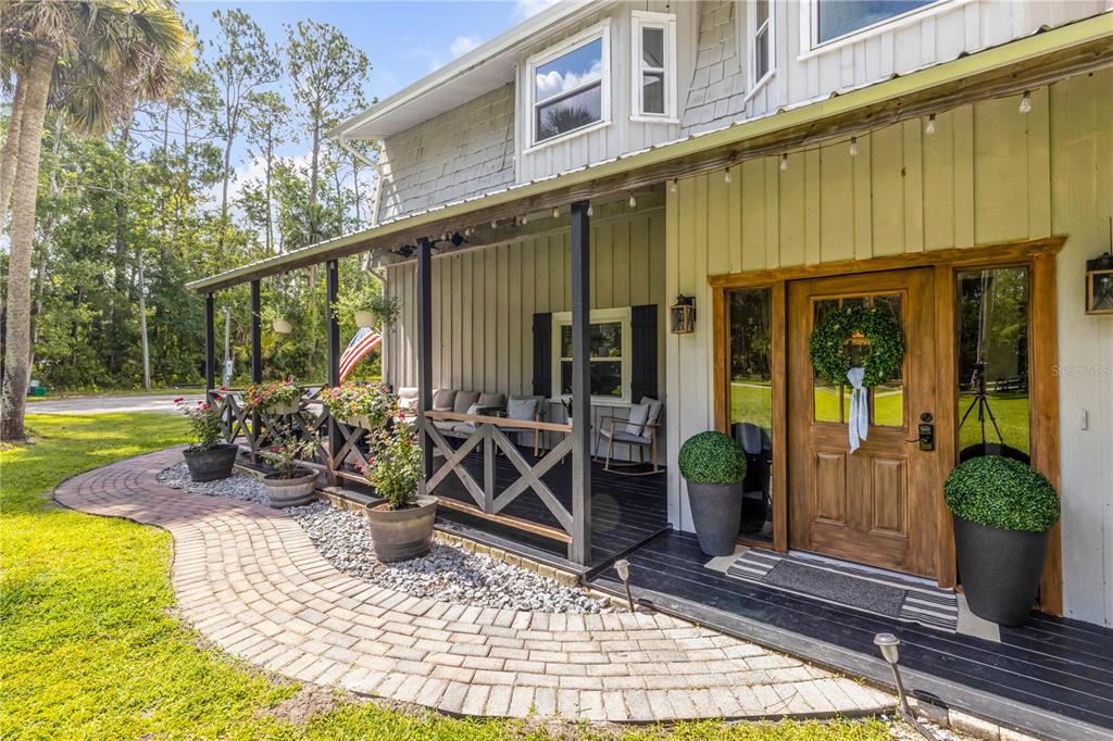 A covered porch with a wooden door, black railing, and brick walkway leads to a house — 2195 W POINSETTIA DRIVE, PORT ORANGE, FL