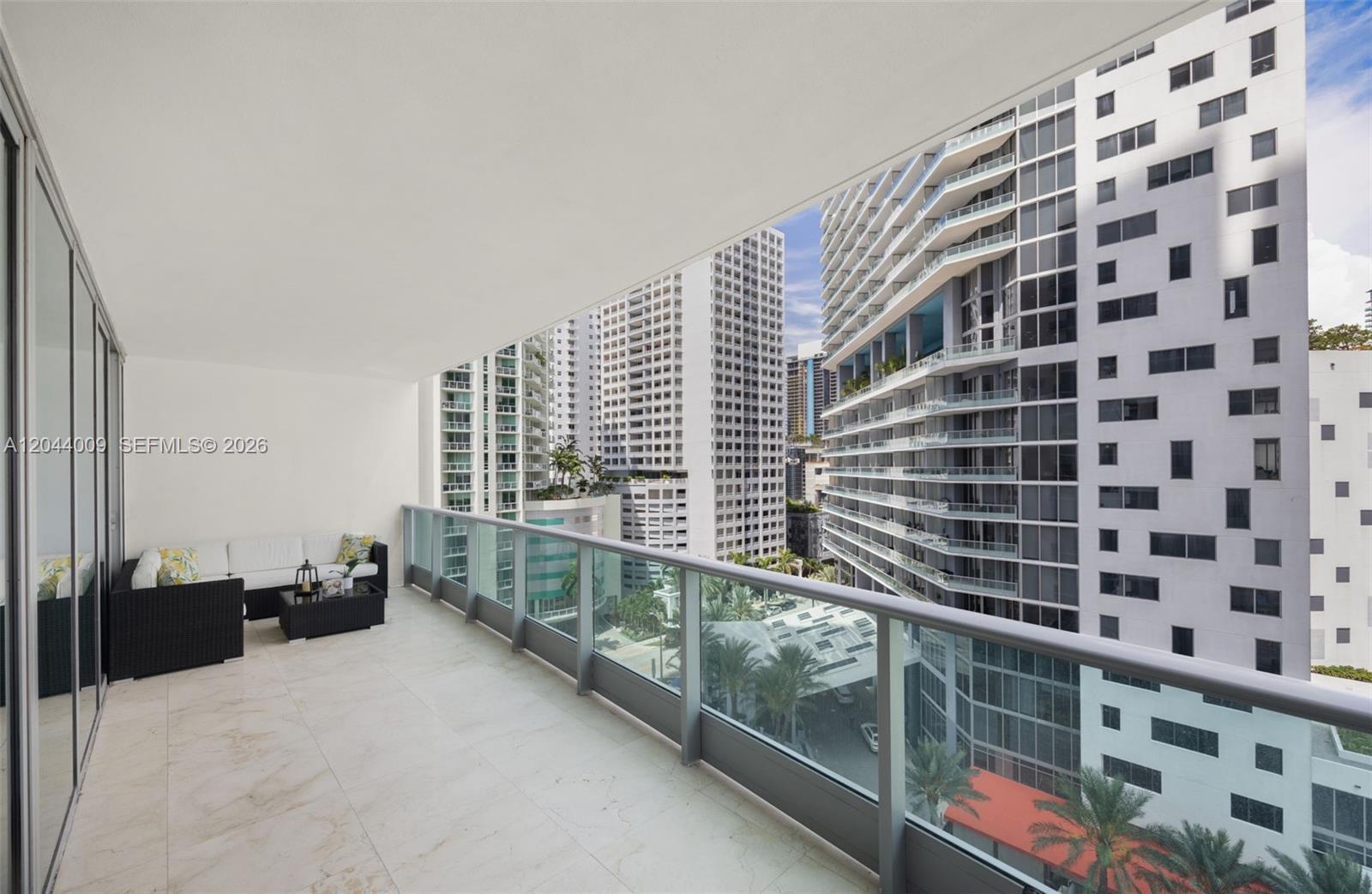 A spacious balcony features white tile flooring, a glass railing, and outdoor seating furniture — 1331 Brickell Bay Dr # 904, Miami FL 33131, MIAMI, FL