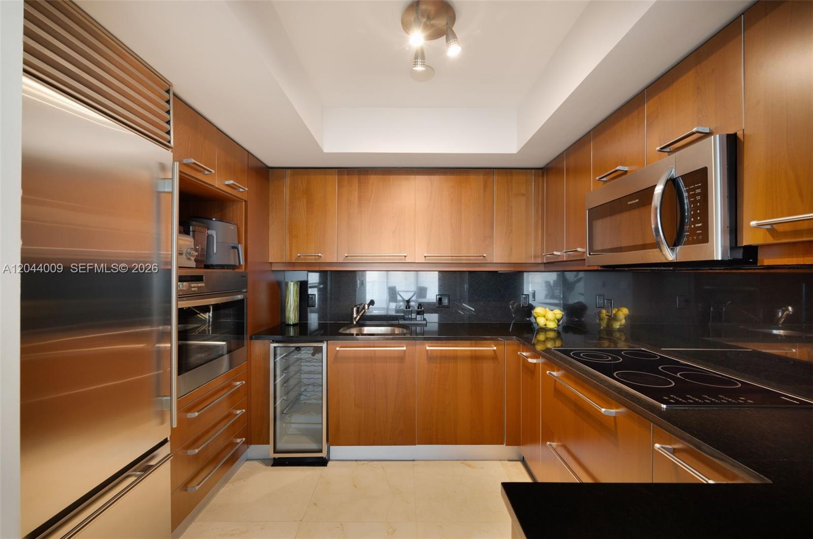 A modern kitchen features wood cabinets, black countertops, stainless steel appliances, and a wine cooler — 1331 Brickell Bay Dr # 904, Miami FL 33131, MIAMI, FL