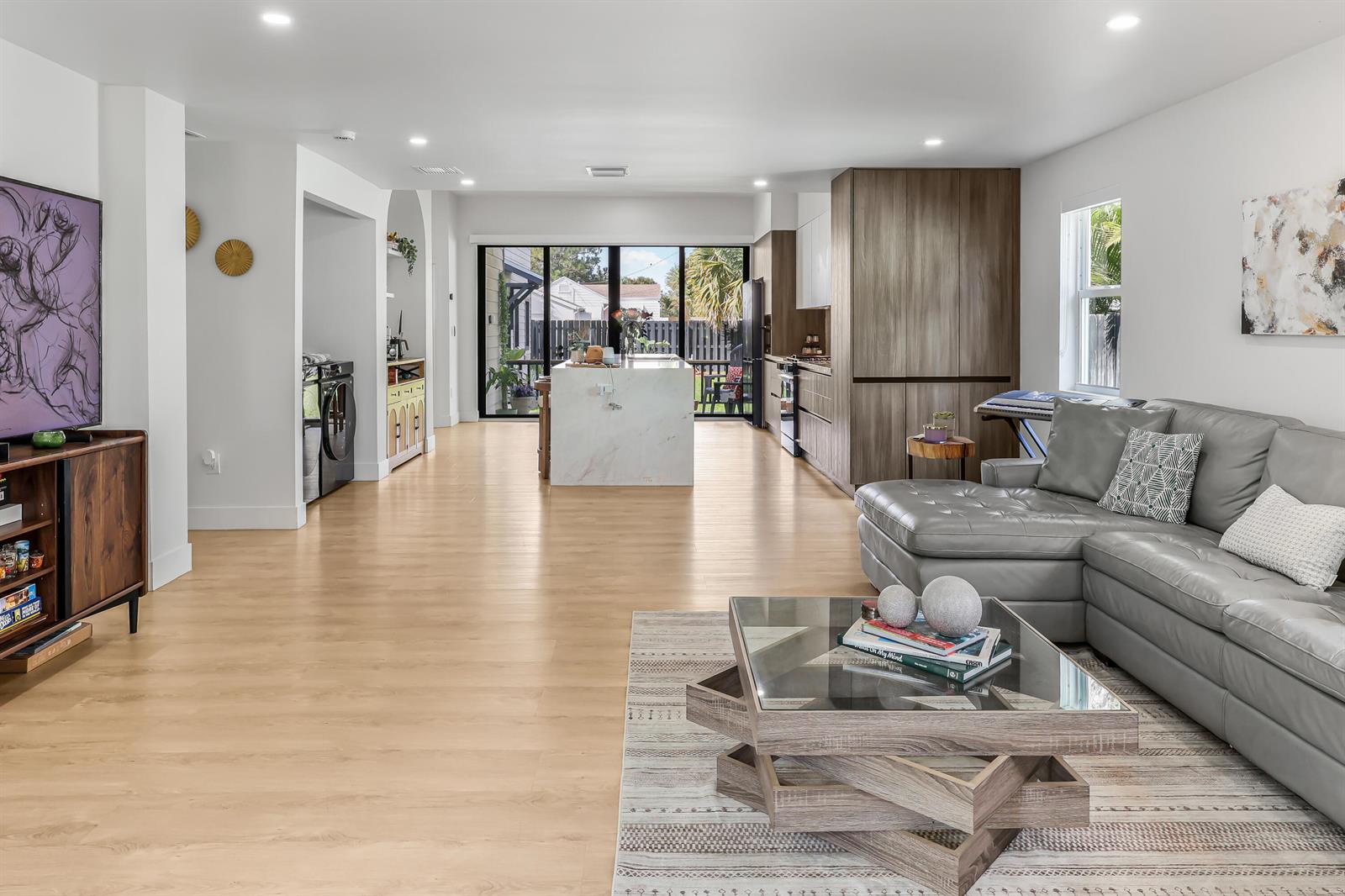 An open-concept living room and kitchen featuring light wood flooring, a marble island, and gray sofa — 1125 N K Street, FL 33460, FL