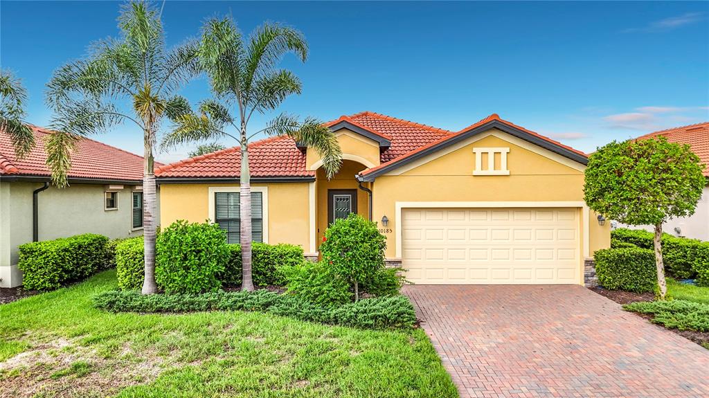 A yellow single-story house features a tile roof, a brick driveway, and palm trees — 10185 COLUBRINA DRIVE, VENICE, FL
