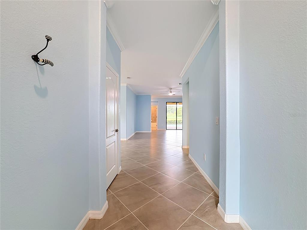 A hallway with light blue walls and diagonal tile flooring leads toward an open living area — 10185 COLUBRINA DRIVE, VENICE, FL