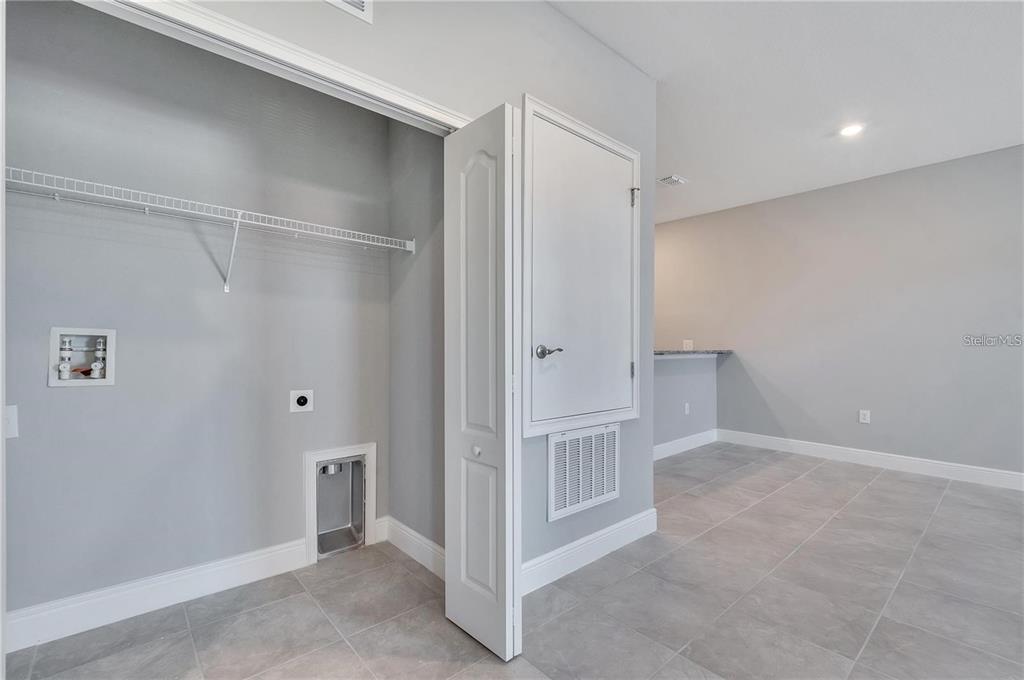 A laundry closet with hookups and a wire shelf sits next to a tiled room — 1803 CORIANDER DRIVE UNIT 1803, POINCIANA, FL