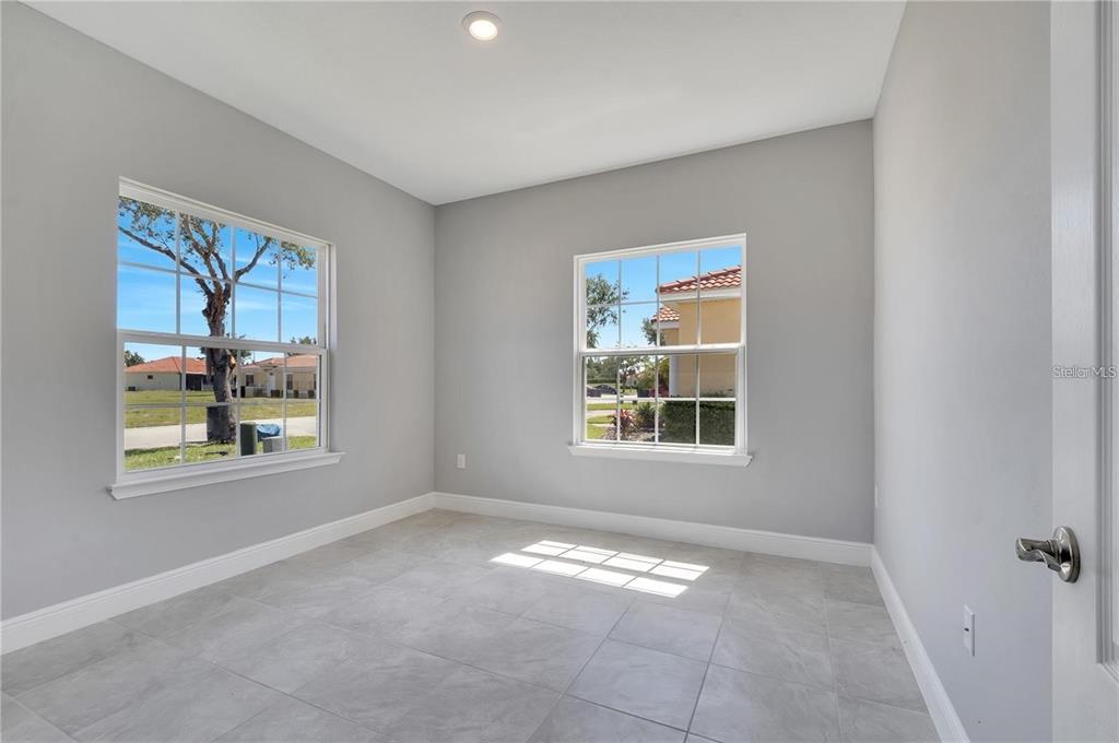 An empty room with gray walls, light tile flooring, and two windows overlooking a neighborhood — 1803 CORIANDER DRIVE UNIT 1803, POINCIANA, FL