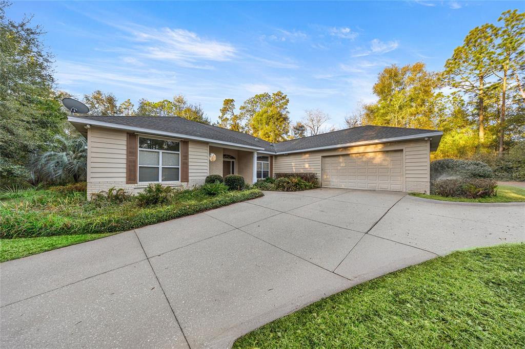 A single-story house with beige siding, a two-car garage, and a large concrete driveway — 20698 SW 93RD LANE ROAD, DUNNELLON, FL