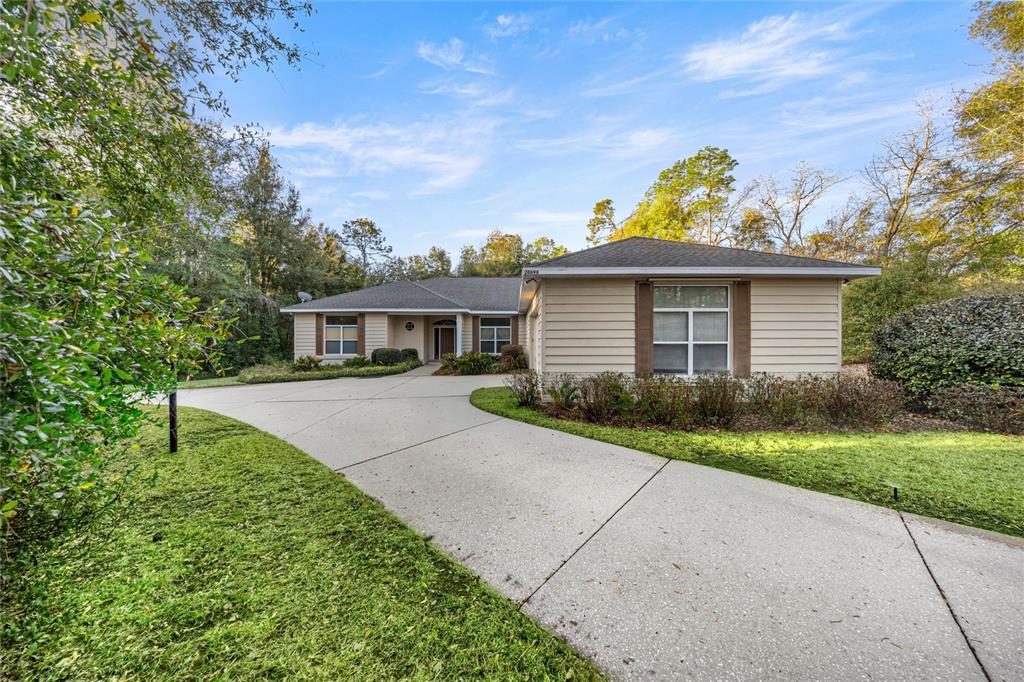 A single-story house with beige siding and a concrete driveway sits among trees — 20698 SW 93RD LANE ROAD, DUNNELLON, FL