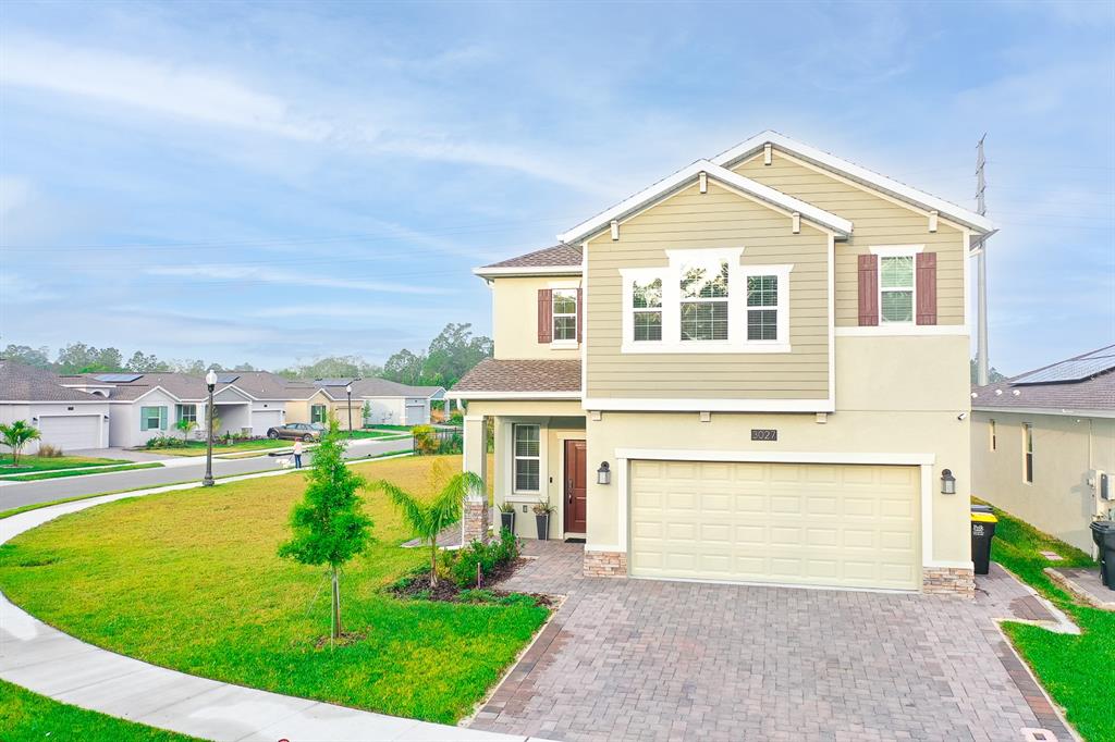 A two-story suburban house with tan siding, a stone-accented entryway, and a paved driveway — 3027 CAMDEN WAY, DAVENPORT, FL