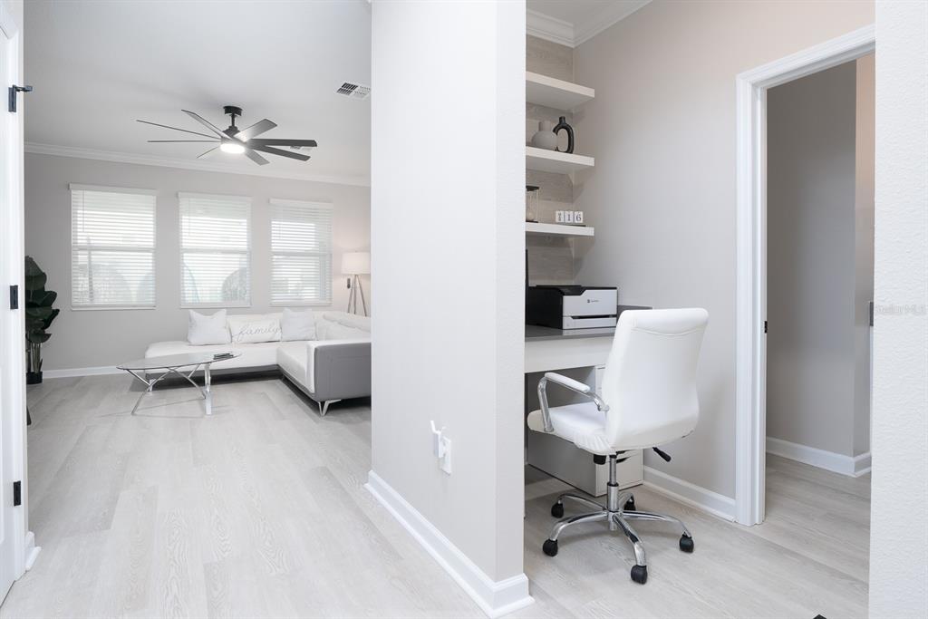 A home office nook with floating shelves sits adjacent to a living room with light flooring — 3027 CAMDEN WAY, DAVENPORT, FL
