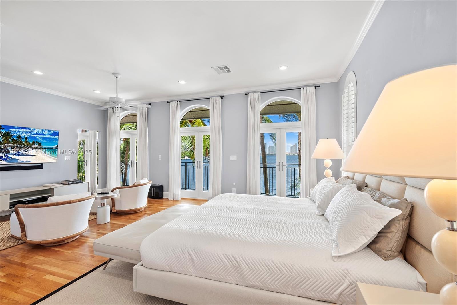 A bedroom features a large bed, seating area, and glass doors overlooking a waterfront view — 814 W Dilido Dr, Miami Beach FL 33139, MIAMI BEACH, FL